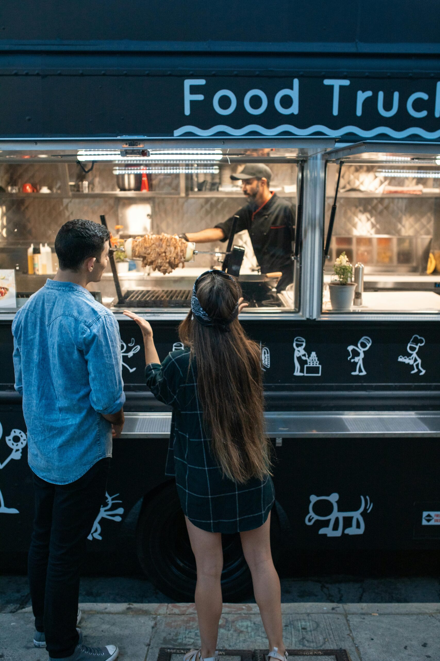 A couple ordering food at a lively street food truck during the day.